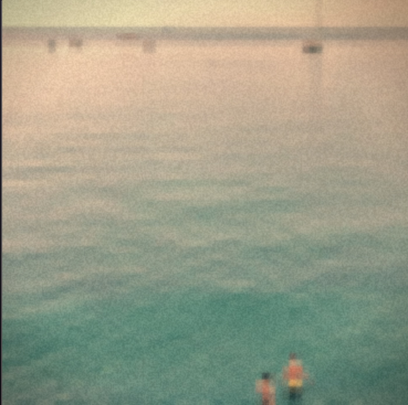A warm faded photograph of two people wading into a vast calm sea, dissolving into grain.