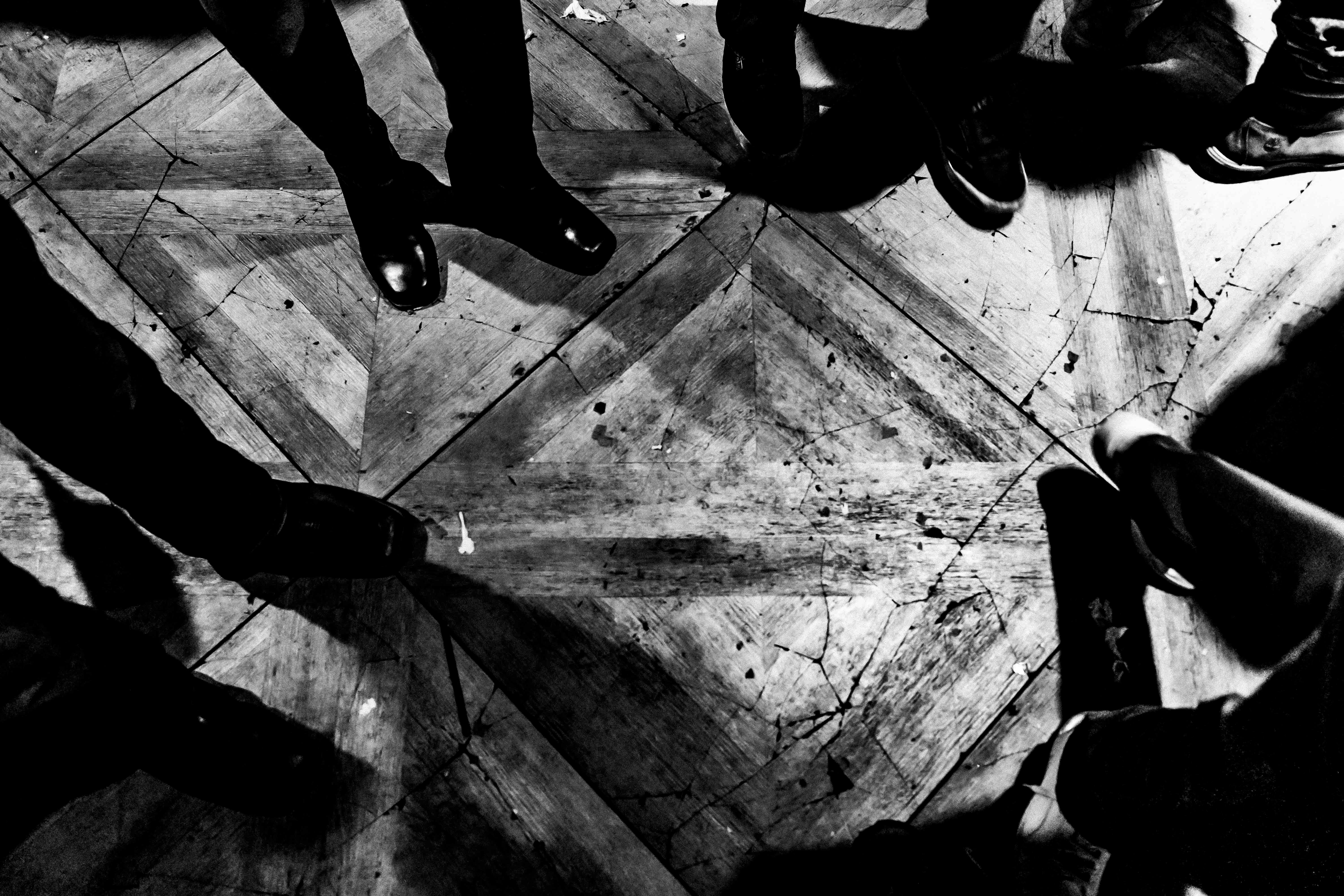 Feet on a scuffed, cracked parquet floor in a dark club, shot from above.